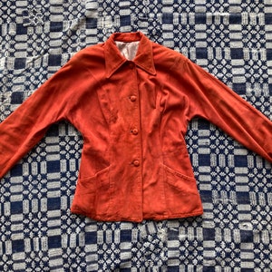 May include: A rust-colored suede jacket with a collared neckline, long sleeves, and button closure. The jacket has two front pockets and a fitted silhouette.