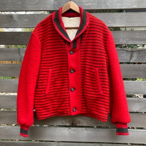 Op de afbeelding: Een rood en zwart gestreept wollen jack met een zwarte kraag en knoopsluiting. Het jack heeft een geribbelde gebreide manchet en zoom.