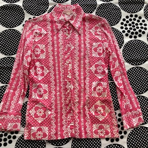 May include: A pink long-sleeve button-up shirt with a white floral pattern. The shirt has a pointed collar and a button-up front.