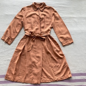 Könnte beinhalten: Ein braunes Kleid mit weißen Punkten und einem passenden Gürtel. Das Kleid hat einen Kragen und lange Ärmel.