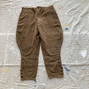 May include: A pair of brown riding breeches with button closures at the bottom of the legs.