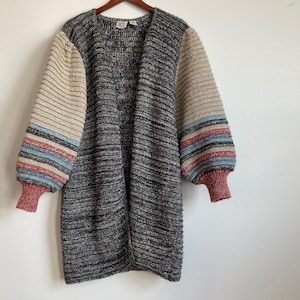 May include: A long, gray cardigan with a ribbed texture. The sleeves are striped with beige, pink, blue, and white.