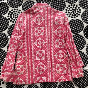 May include: A pink and white patterned long-sleeve shirt with a button-up collar. The shirt has a floral design with a repeating pattern.