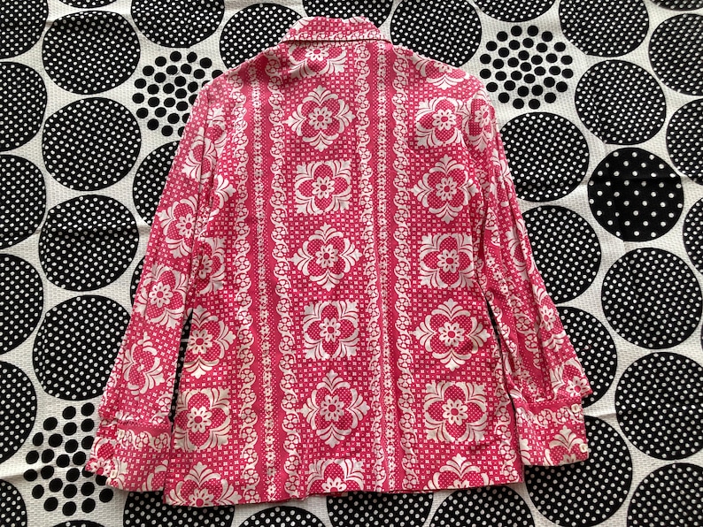 May include: A pink and white patterned long-sleeve shirt with a button-up collar. The shirt has a floral design with a repeating pattern.