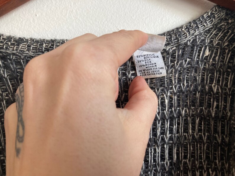 May include: A black and white knit sweater with a white tag that reads "$21% Acrylic, 38% Silk, 10% Mohair. See reverse for care. Voir au verso pour entretien."