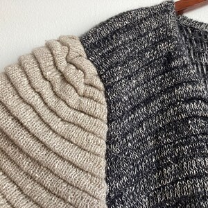 May include: A beige and black knitted cardigan with a ribbed texture. The cardigan has a V-neck and a long sleeve. The brand name "Born Bill" is visible on the tag.
