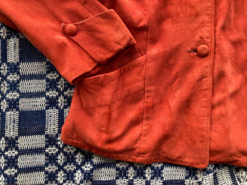 May include: A rust-colored suede jacket with a button closure and a pocket on the left side.