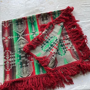 May include: A gray and white blanket with red, green, and brown geometric patterns. The blanket has a fringe border with red tassels.