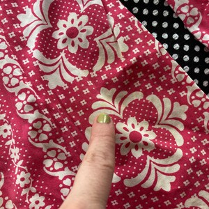 May include: Close-up of a pink fabric with a white floral pattern. The fabric has a small white dot pattern on a pink background.