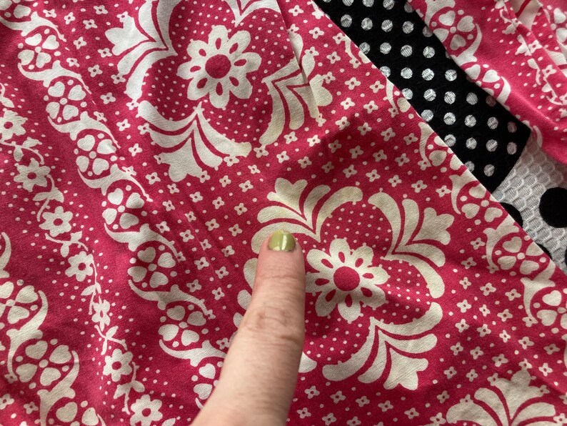 May include: Close-up of a pink fabric with a white floral pattern. The fabric has a small white dot pattern on a pink background.