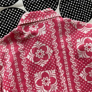 May include: A pink and white patterned shirt with a collar. The pattern features a repeating floral design.