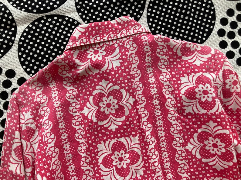 May include: A pink and white patterned shirt with a collar. The pattern features a repeating floral design.