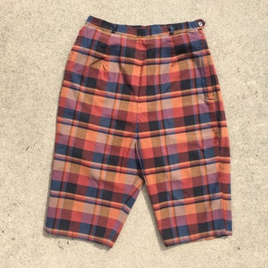 May include: A pair of plaid shorts in shades of orange, red, blue, and black. The shorts have a button and zipper closure and side pockets.