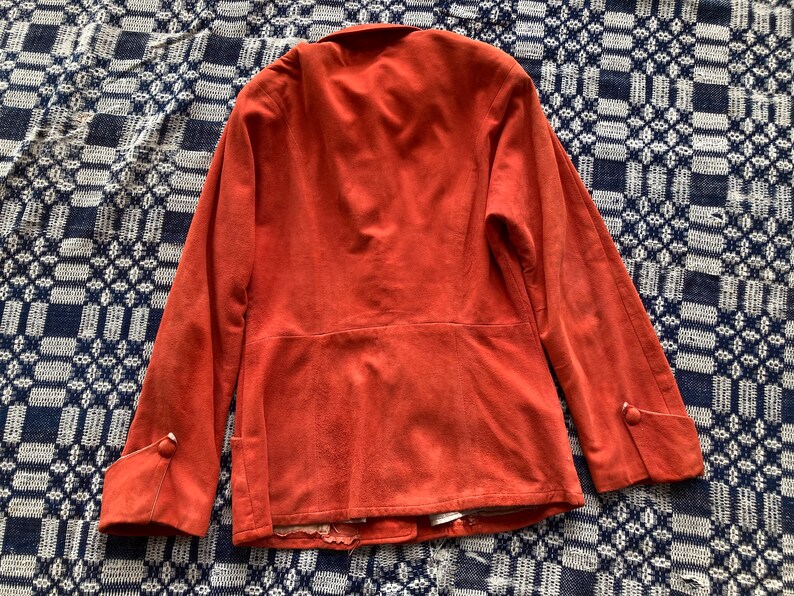 May include: A rust-colored suede jacket with long sleeves and buttoned cuffs. The jacket has a simple design and a slightly fitted silhouette.