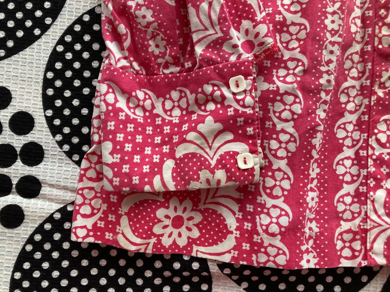 May include: Pink and white patterned fabric with white buttons. The fabric has a floral design.