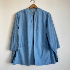 May include: A light blue long-sleeved jacket with a stand-up collar and a zipper closure. The jacket has two pockets on the front and a label that says "Lafayette Collection" on the inside.