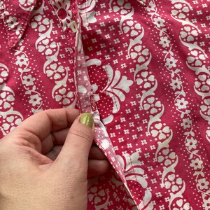 May include: Close-up of a pink and white patterned fabric with a button and a seam. The fabric has a floral design with small white flowers and a larger white floral pattern.