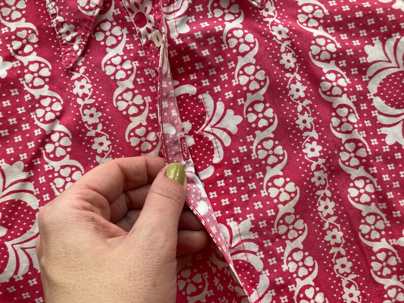 May include: Close-up of a pink and white patterned fabric with a button and a seam. The fabric has a floral design with small white flowers and a larger white floral pattern.