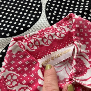 May include: A pink and white patterned shirt with a white label that reads "Koret of California".