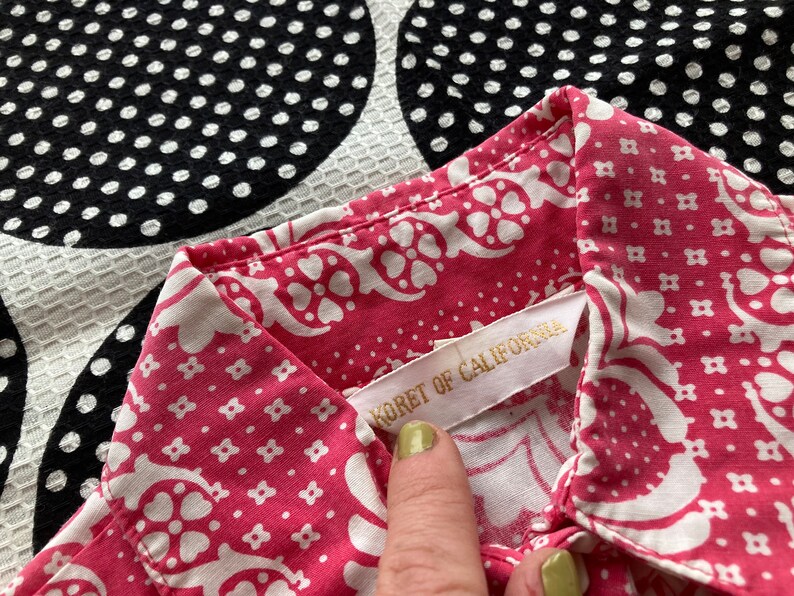 May include: A pink and white patterned shirt with a white label that reads "Koret of California".