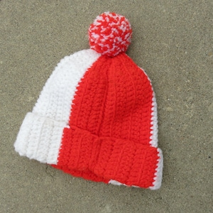 May include: A red and white crocheted beanie with a white pom-pom on top.
