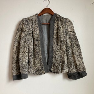 May include: A gray and white patterned cardigan with a shawl collar and long sleeves. The cardigan has a gray lining and is open in the front.