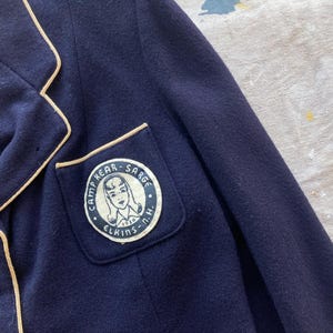 Może przedstawiać: Granatowa marynarka z kremową lam&oacute;wką i naszywką na lewej piersi z napisem "Camp Kear - Sarge Elkins - N.H."