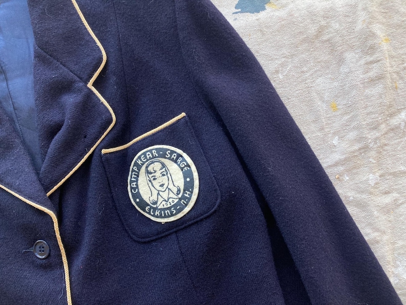 Może przedstawiać: Granatowa marynarka z kremową lam&oacute;wką i naszywką na lewej piersi z napisem "Camp Kear - Sarge Elkins - N.H."