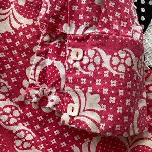 May include: Close-up of a pink fabric with a white floral pattern. The fabric has two white buttons on the cuff.