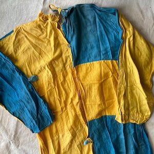 Puede incluir: Una camisa de algodón amarilla y azul con cierre de botones en la parte delantera y mangas largas. La camisa está hecha de una tela ligera y tiene un corte holgado.