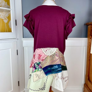 May include: A maroon t-shirt with ruffled sleeves and a patchwork skirt made from various fabrics, including lace, paisley, and floral prints.