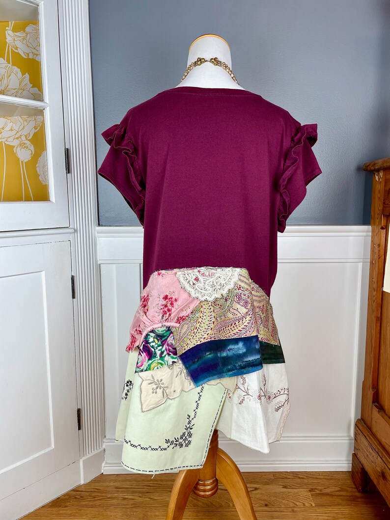 May include: A maroon t-shirt with ruffled sleeves and a patchwork skirt made from various fabrics, including lace, paisley, and floral prints.