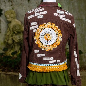 May include: Brown corduroy jacket with a crocheted doily on the back. The jacket is decorated with various fabric scraps with handwritten text, including "the sun that makes armholes" and "full of beauty".