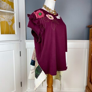 May include: A burgundy t-shirt with a floral design on the shoulder and a patchwork skirt attached to the bottom.