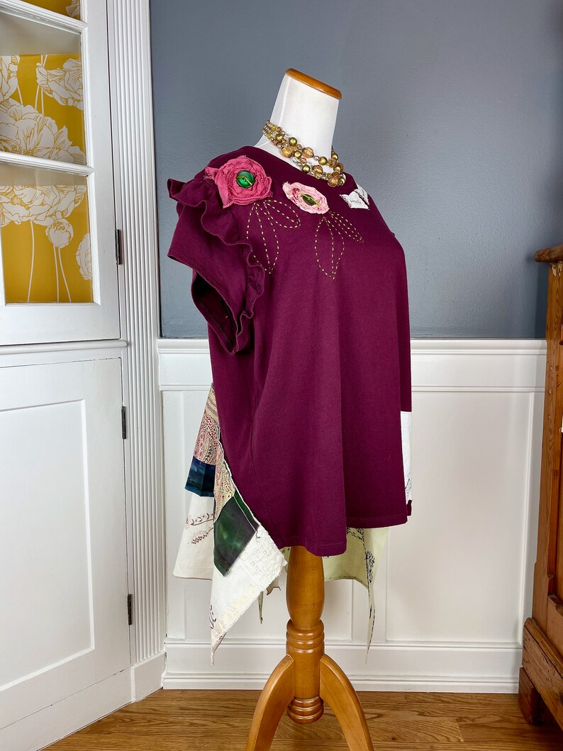 May include: A burgundy t-shirt with a floral design on the shoulder and a patchwork skirt attached to the bottom.