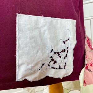 May include: A burgundy fabric with a white linen pocket featuring a delicate white embroidered floral design.