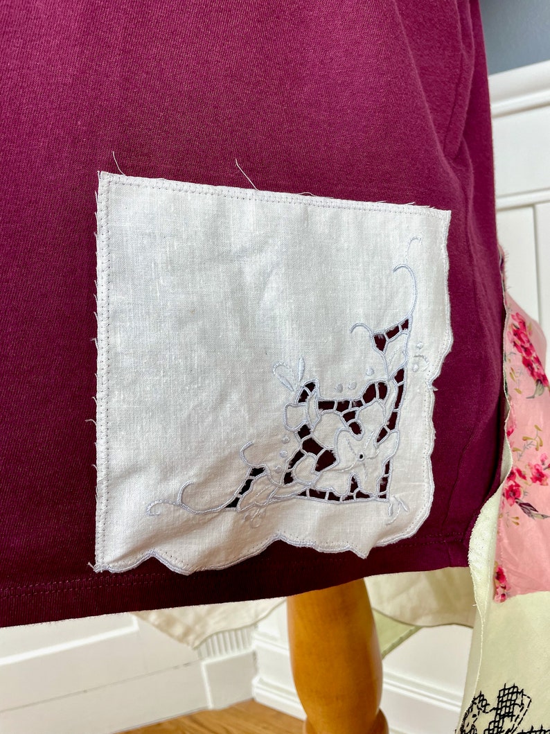 May include: A burgundy fabric with a white linen pocket featuring a delicate white embroidered floral design.