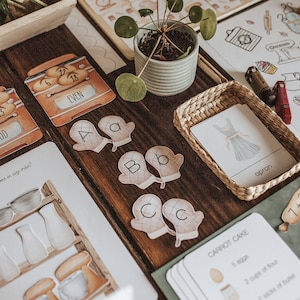 Puede incluir: Un conjunto de tarjetas educativas para niños con una variedad de temas, que incluyen números, letras, repostería y ropa. Las tarjetas son coloridas y presentan ilustraciones de varios objetos. Las tarjetas están dispuestas sobre una mesa de madera con una pequeña planta en maceta.