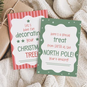 May include: Two Christmas gift tags with festive text. One tag has a red and white striped border with the text "Let's have fun decorating your CHRISTMAS TREE!". The other tag has a green border with the text "here's a special treat from SANTA at the NORTH POLE!"