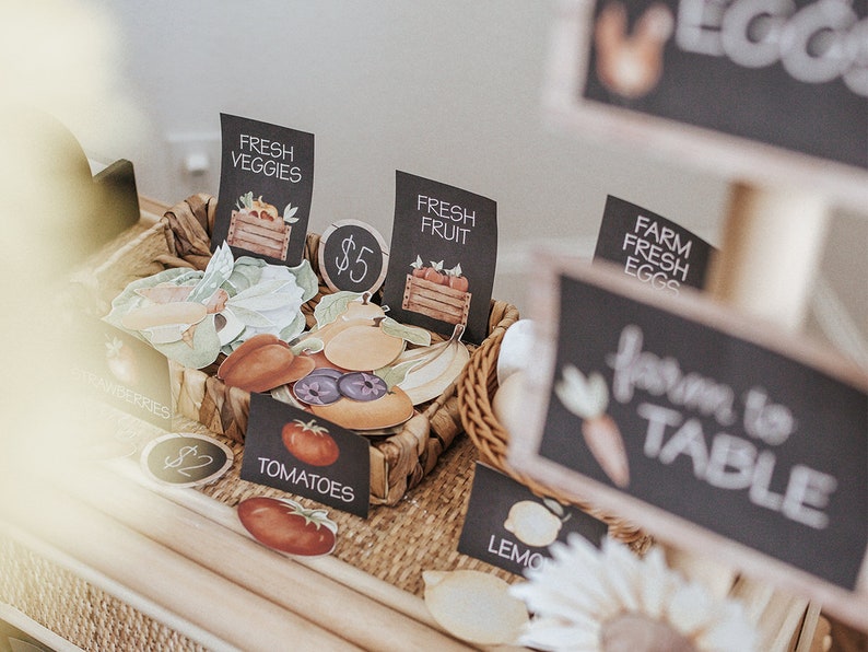 May include: A wicker basket filled with paper cutouts of fresh produce, including tomatoes, lemons, and blueberries. Black chalkboard signs display the words "Fresh Veggies," "Fresh Fruit," and "Farm Fresh Eggs."