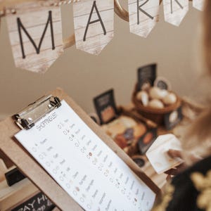 May include: A market scene with a wooden banner that reads "MARKET". A clipboard with a shopping list is in the foreground. The list includes items like honey, eggs, and cheese. A person is holding a piece of cheese.