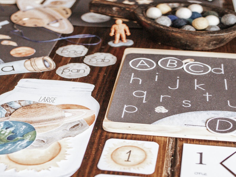 May include: A set of educational materials for children, including a chalkboard with the alphabet, a jar with planets, and cards with numbers and words. The materials are designed to help children learn about the solar system and the alphabet.