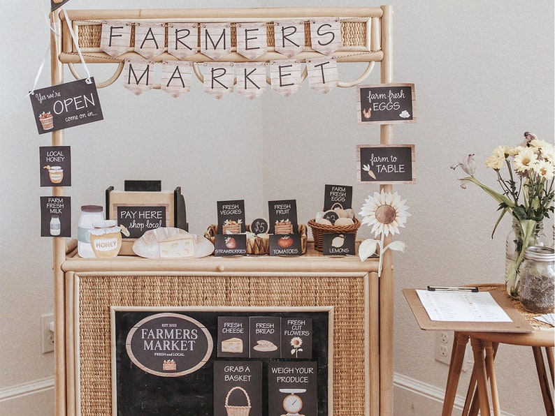 May include: A farmers market stall made of woven wood, with signs advertising fresh produce, honey, and eggs. The stall has a chalkboard sign with the words "Farmers Market" and a banner that reads "Farmers Market".