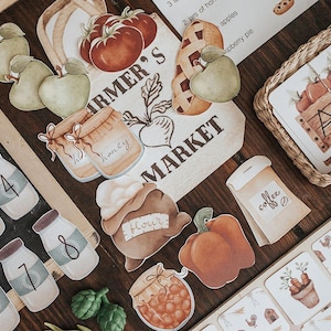 Può includere: Una collezione di ritagli di carta in stile acquerello a tema mercato degli agricoltori. Include mele, pomodori, barattoli di miele, una zucca e un sacchetto di caffè. Il testo "Farmer's Market" è visibile.