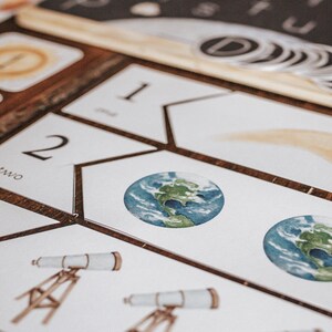 May include: A set of white cards with numbers and images of a comet, earth, and a telescope. The cards are arranged in a pattern on a wooden surface.
