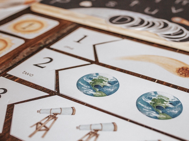 May include: A set of white cards with numbers and images of a comet, earth, and a telescope. The cards are arranged in a pattern on a wooden surface.