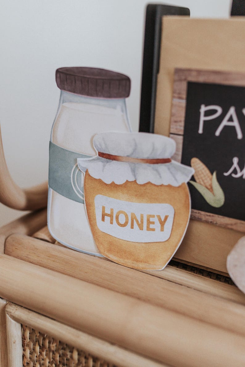 May include: Watercolour illustration of a milk bottle with a brown lid and a honey jar with a white lid and the word "HONEY". The jars are on a wooden surface.