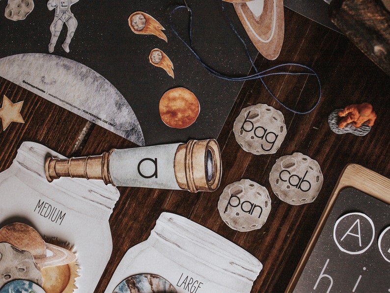 May include: A set of space-themed educational materials for children, including a telescope, a moon with the word "bag" on it, a moon with the word "cab" on it, a moon with the word "pan" on it, and a chalkboard with the letters "A" and "hi" on it.