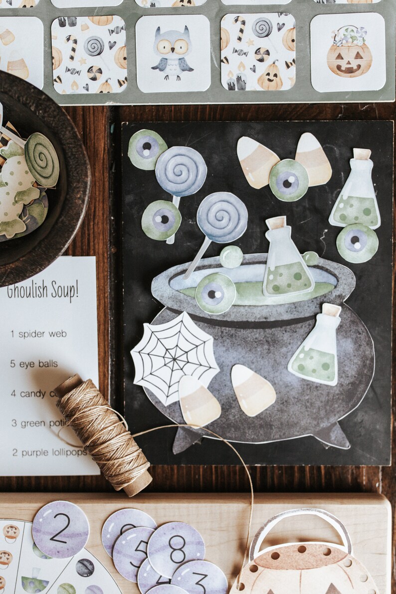 May include: A collection of Halloween-themed paper cutouts and craft supplies. Includes a cauldron, potion bottles, candy corn, lollipops, and an owl. A list titled "Ghoulish Soup!" is also present, along with twine and number cutouts. The color palette is muted with shades of gray, green, and orange.