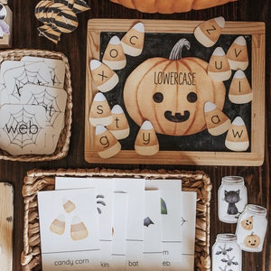 May include: A Halloween-themed educational set with a pumpkin, candy corn, and alphabet letters. The set includes flashcards with words like "web" and "candy corn", and decorative jar cutouts. The word "lowercase" is written on the pumpkin.